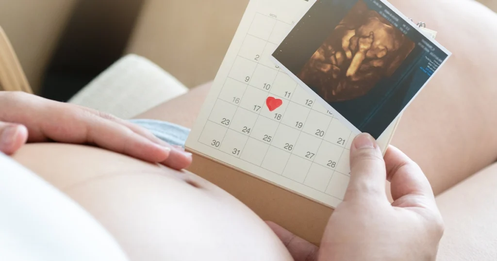 Pregnant woman holding a calendar with a red heart marking the due date alongside a baby ultrasound scan image, representing factors that affect pregnancy due date accuracy