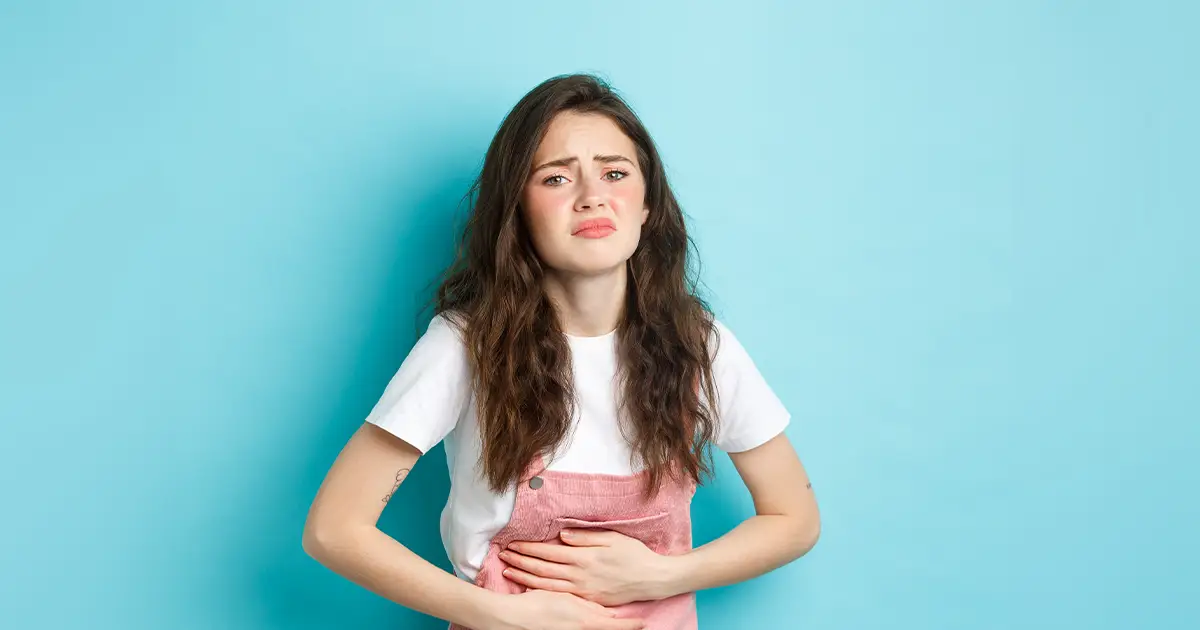 Woman holding stomach in discomfort, illustrating PCOS belly symptoms and abdominal pain from polycystic ovary syndrome