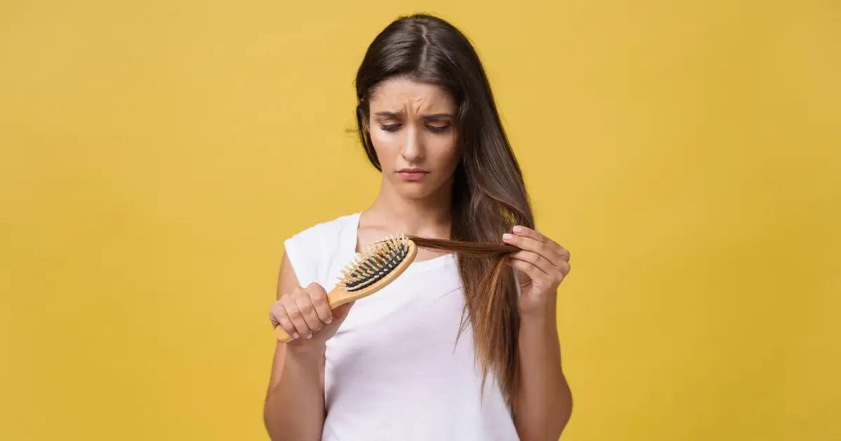 Woman looking at hair loss in brush — hormonal hair loss in women