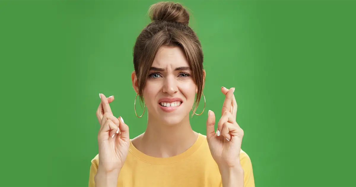 Anxious woman with crossed fingers showing nervous hopeful expression from hormone mood swings.